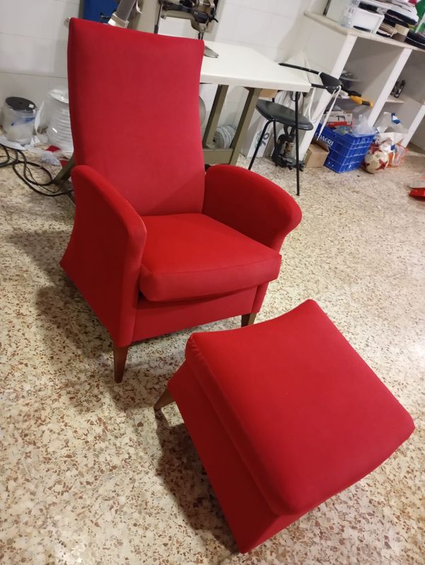 Sillón orejero de respaldo alto retapizado en rojo, con reposapiés